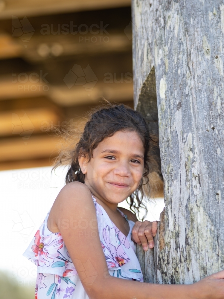 Indigenous girl standing against a wooden pole - Australian Stock Image
