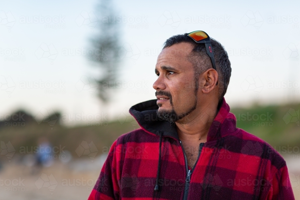 Indigenous man gazing out of frame with sunnies on head - Australian Stock Image