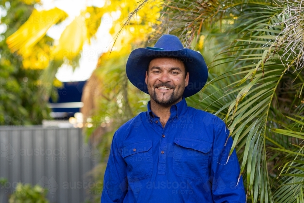 indigenous man outdoors smiling and wearing blue hat and blue shirt - Australian Stock Image
