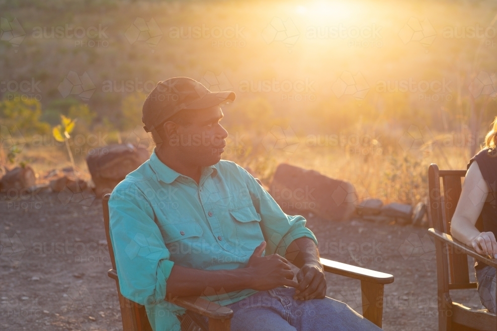 Indigenous man sitting outdoors at sunset - Australian Stock Image