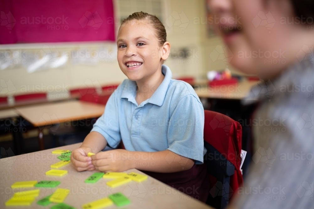 Indigenous primary school student smiling working with coloured word tiles - Australian Stock Image