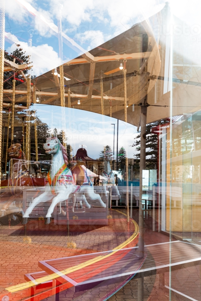 Indoor carousel behind rounded glass window with reflection of outdoors in Glenelg South Australia - Australian Stock Image