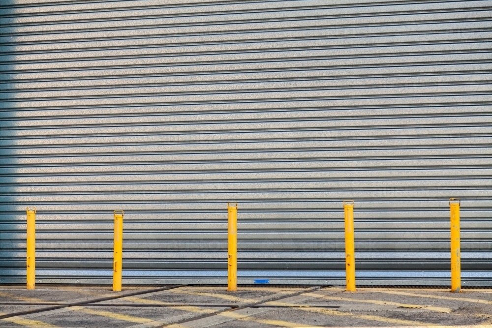 Industrial metal roller door with yellow posts blocking entry - Australian Stock Image