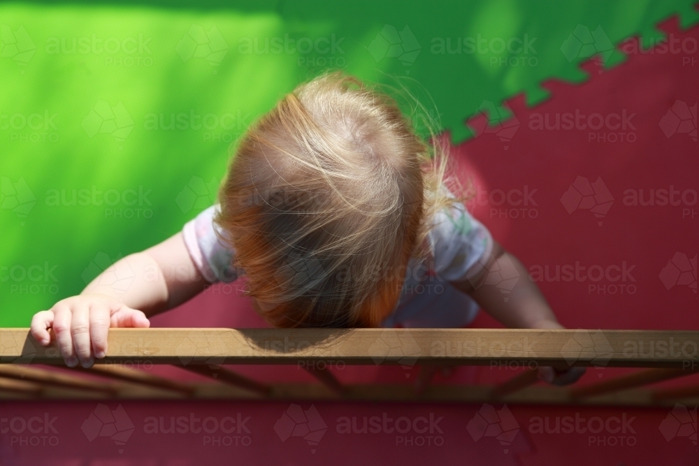 Infant standing and holding on to playpen in garden. - Australian Stock Image