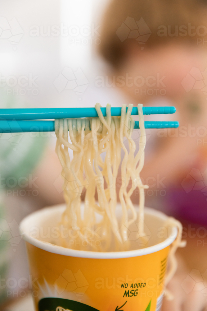 instant ramen noodles being lifted from a paper cup using chopsticks - Australian Stock Image