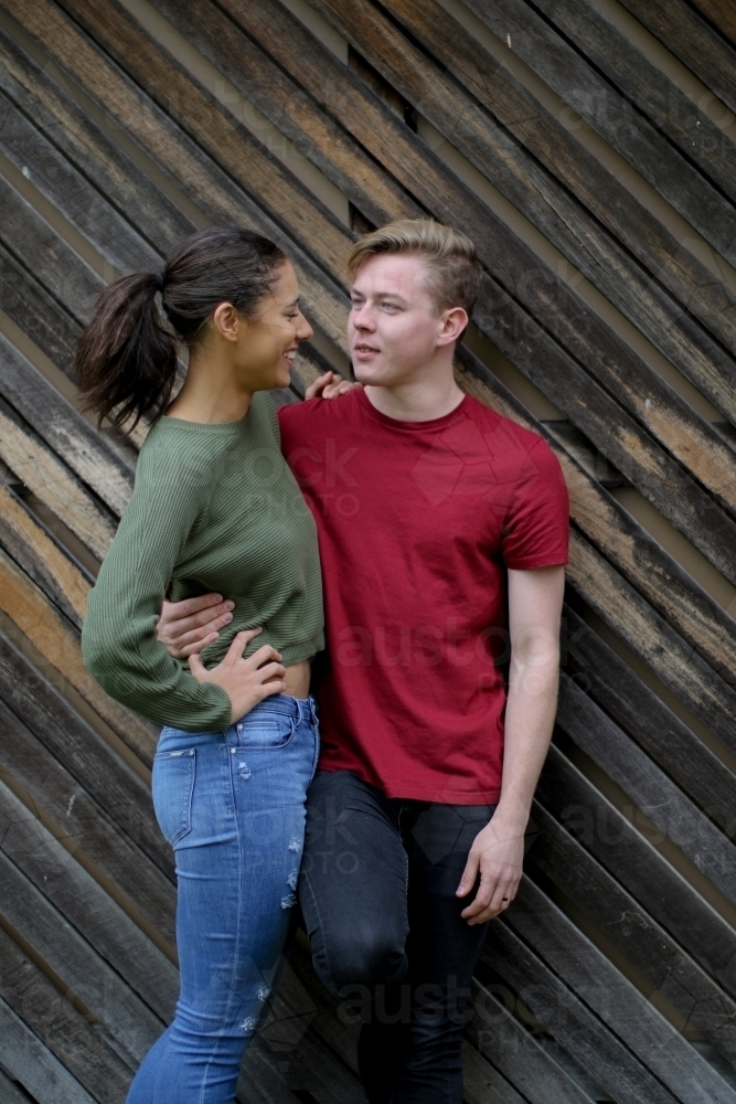 Interracial couple chatting whilst leaning up against a wooden panelled wall - Australian Stock Image
