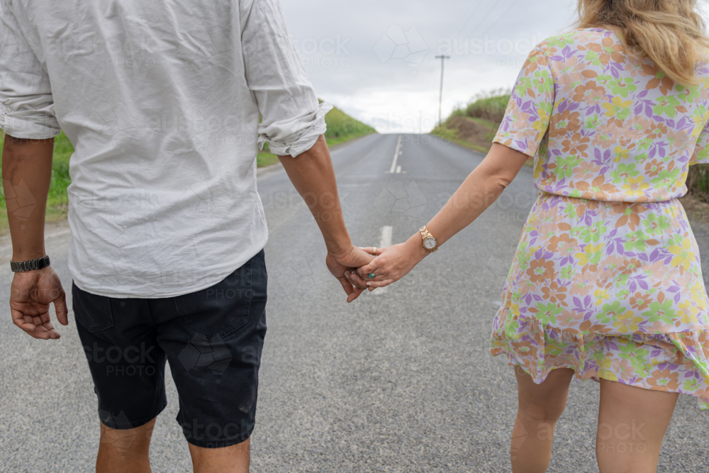 Interracial couple holding hands while walking on a road - Australian Stock Image