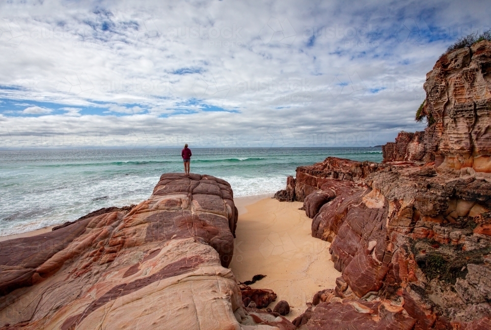 Iron rich red rocks with sandstone offer a dramatic landscape along the coastline beaches Eden - Australian Stock Image