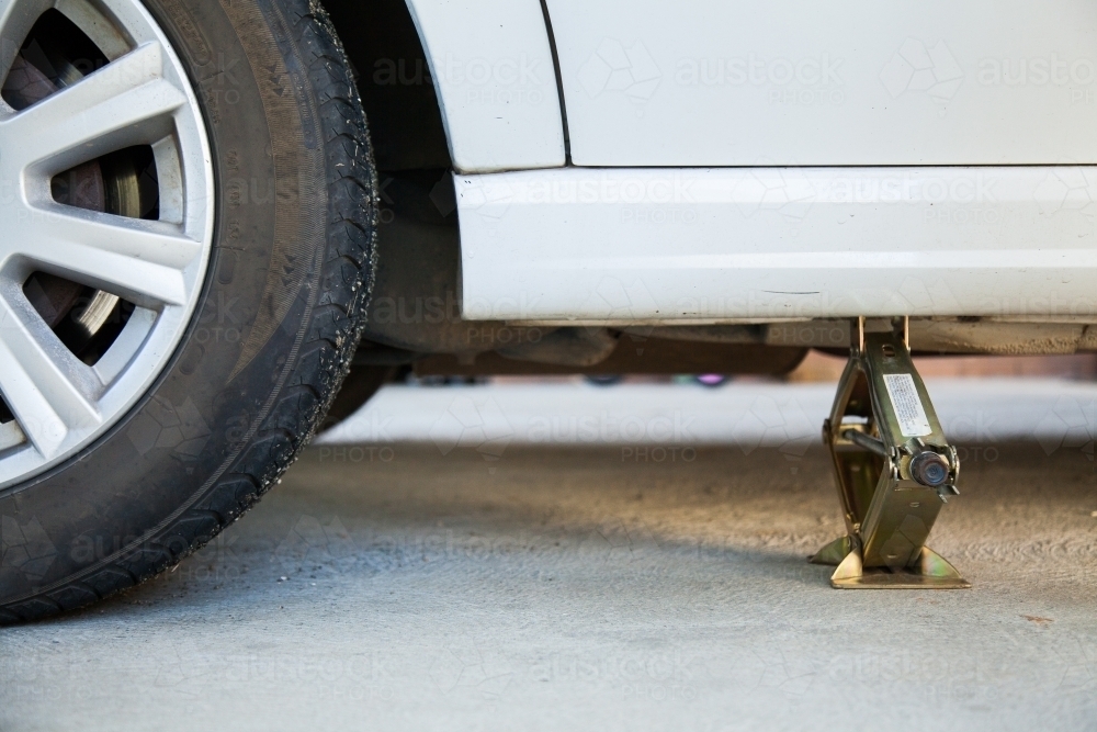 Jacking up car to change flat tyre with small hand jack - Australian Stock Image