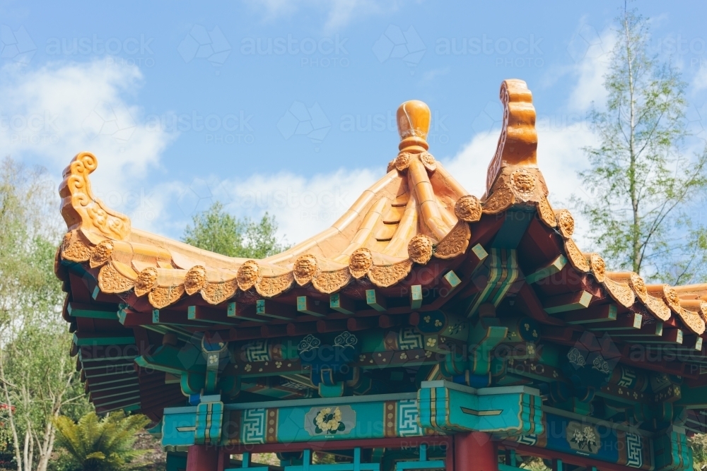 Japanese style golden coloured rotunda roof with trees, blue sky and clouds in the background - Australian Stock Image