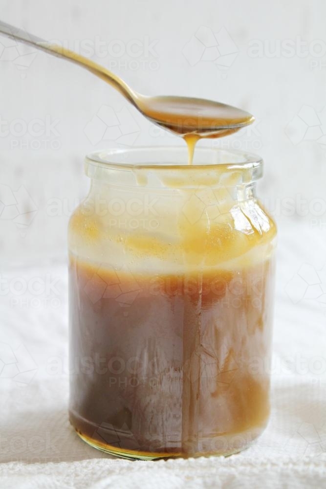 Jar of caramel sauce with spoon dripping - Australian Stock Image