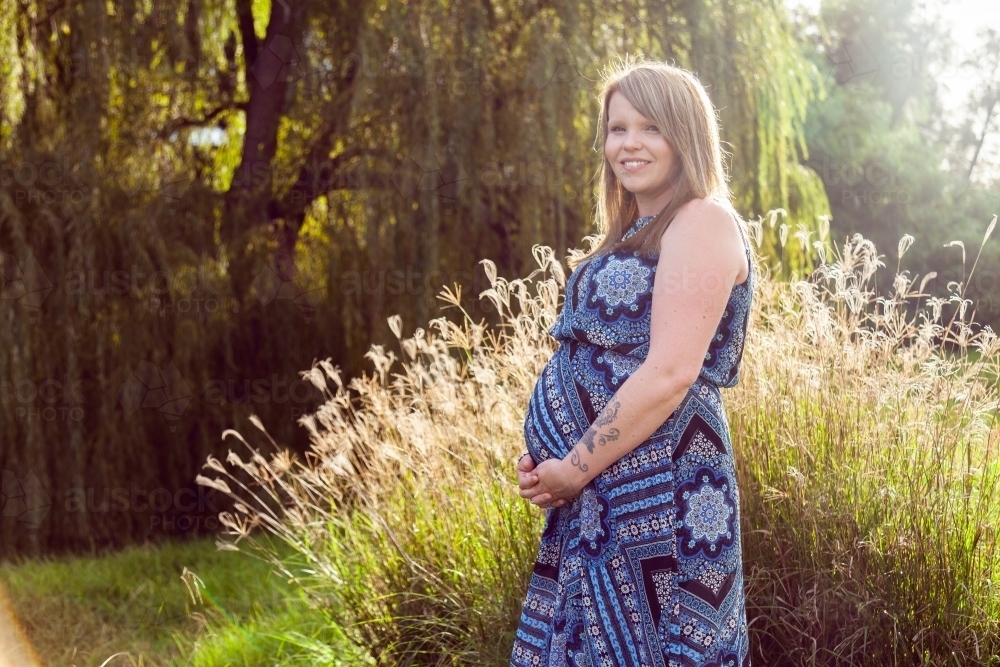 Joyful expectant mother sunlit, standing in nature - Australian Stock Image