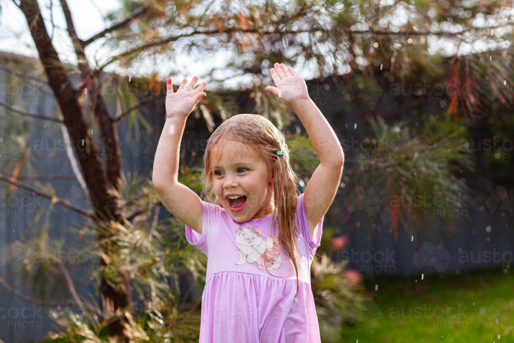 Joyful kid dancing in the rain in Australian backyard among native bushes  - Australian Stock Image