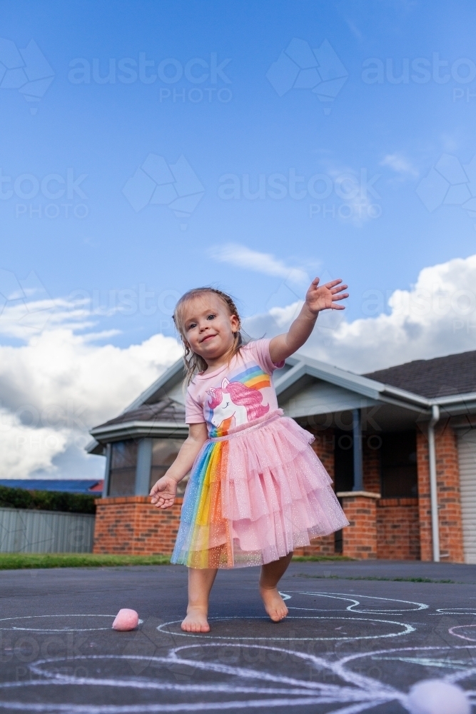 Joyful little girl in sparkly dress dancing outside home - Australian Stock Image