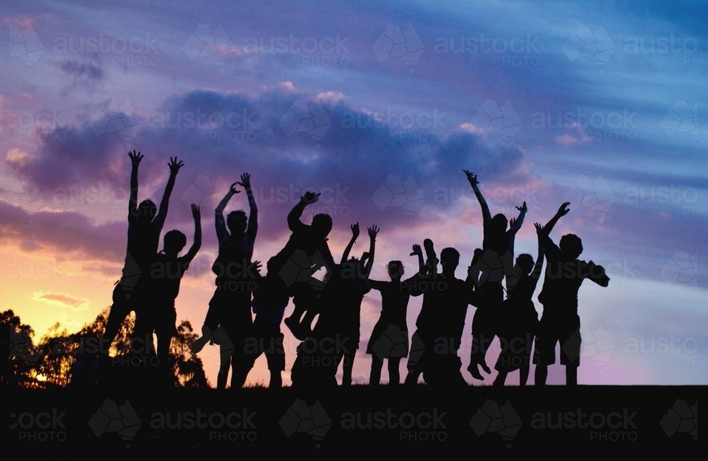 Jumping people on a hilltop silhouetted at sunset - Australian Stock Image
