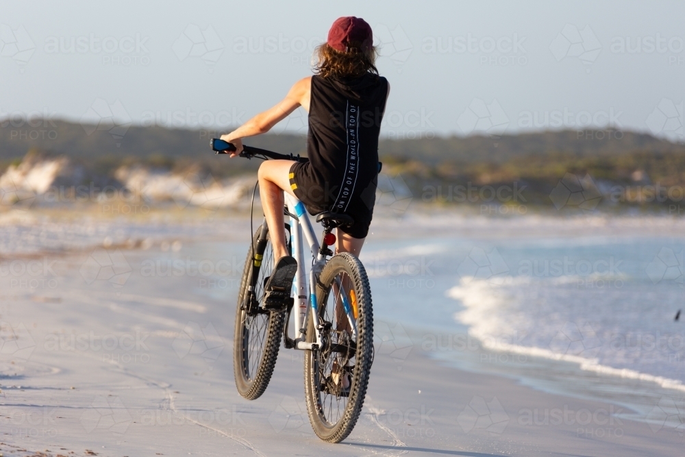 Kid doing a wheelie on bike on beach - Australian Stock Image