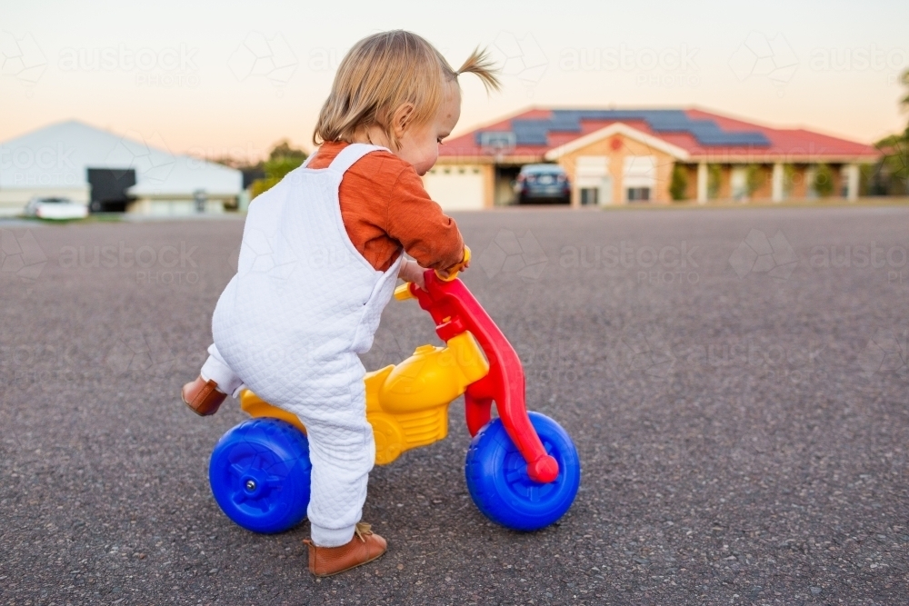 Image of Kid getting onto red yellow and blue plastic trike - Austockphoto