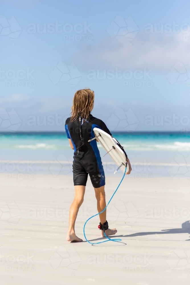 Kid heading out to the waves with his surfboard - Australian Stock Image