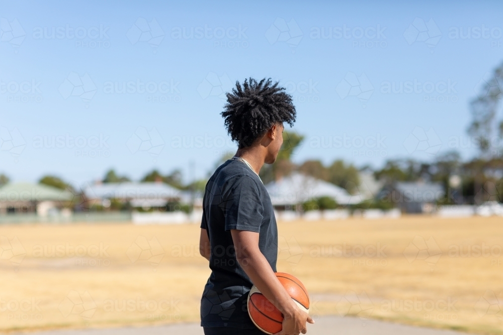 kid in black looking away holding basketball - Australian Stock Image