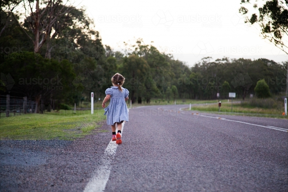 Kid in dress running down rural road - Australian Stock Image