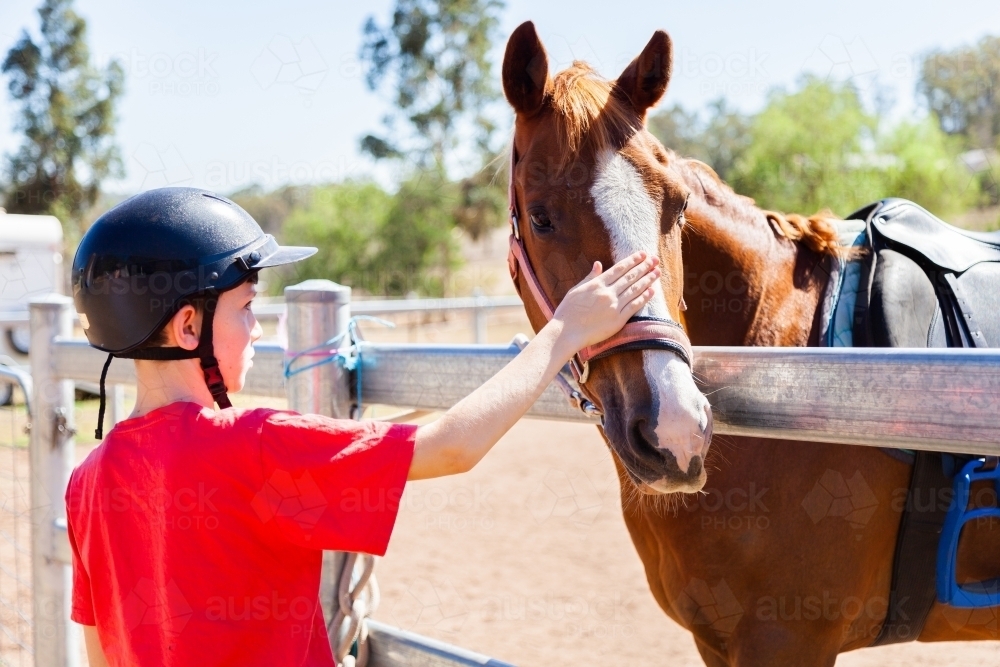 Kid in helmet patting horse over fence getting ready for riding lesson - Australian Stock Image