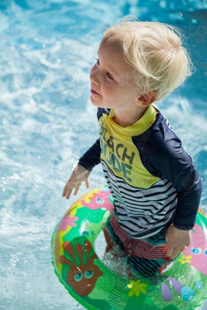 Kid in inflatable swimming ring standing in pool - Australian Stock Image