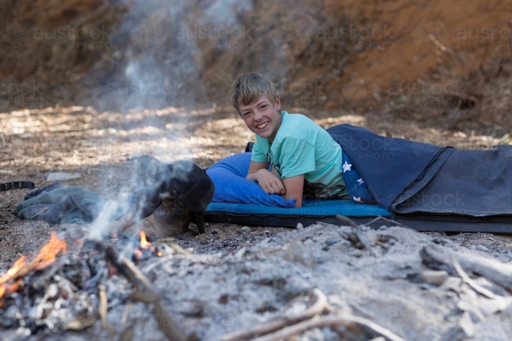Kid in swag near campfire - Australian Stock Image