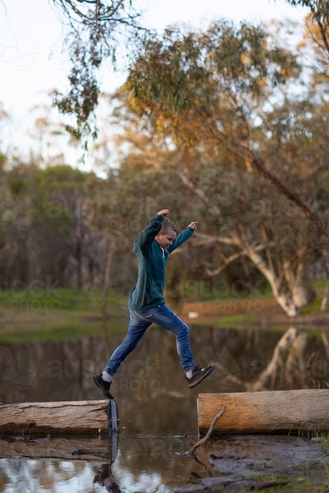 kid jumping between logs on a riverbank - Australian Stock Image