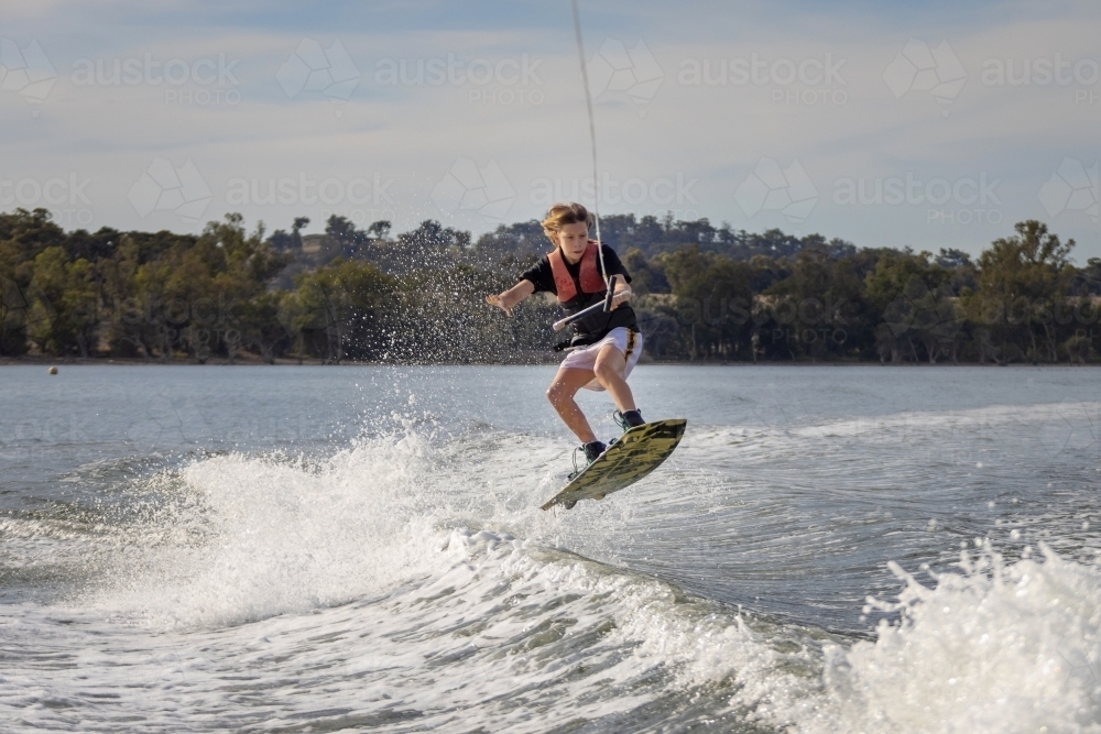 kid jumping wake on wakeboard on inland lake - Australian Stock Image