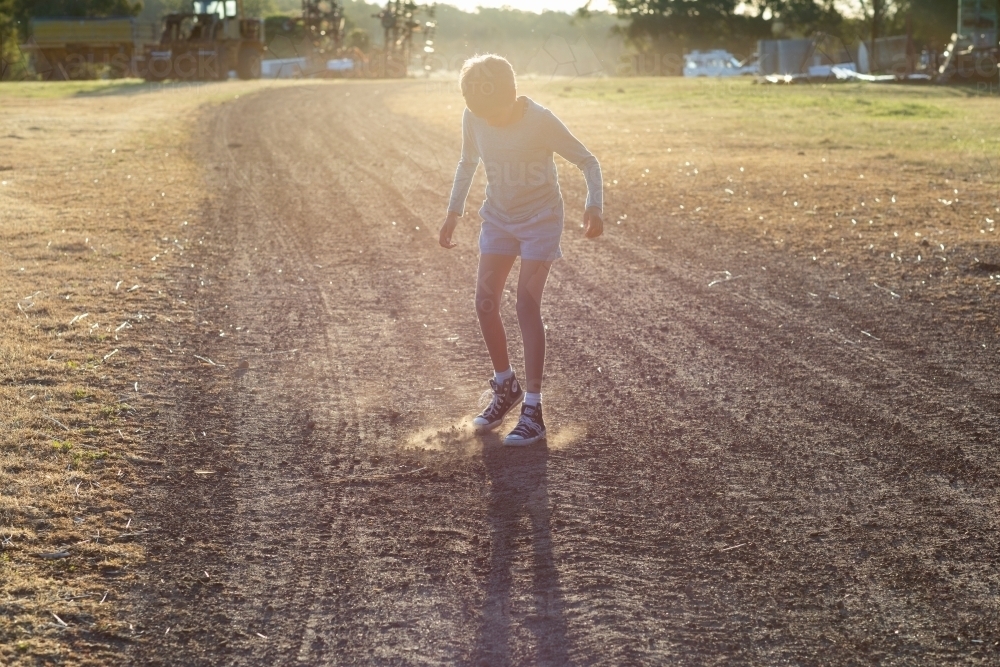 kid kicking up dust on rural farm track - Australian Stock Image
