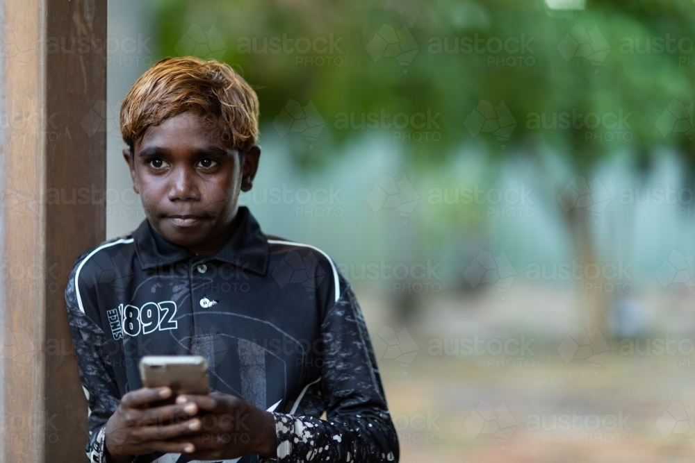 kid leaning against a post with mobile phone in hands - Australian Stock Image