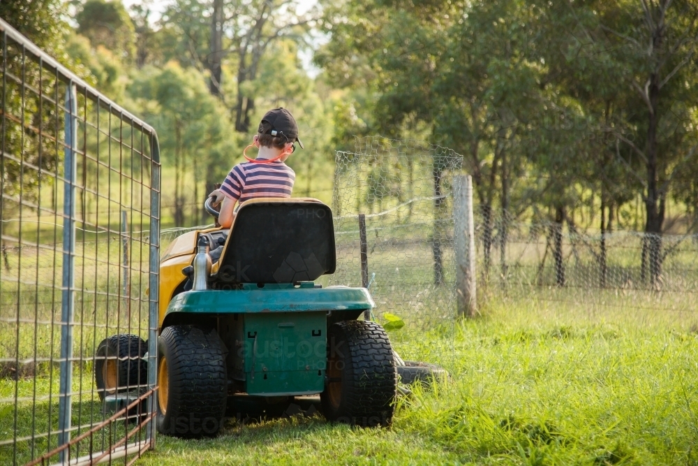 Kid mowing the backyard on a ride on lawn mower - Australian Stock Image