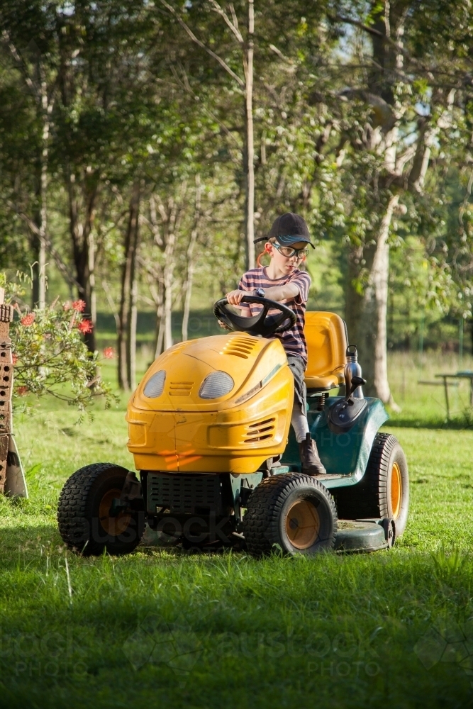 Kid mowing the backyard on a ride on lawn mower - Australian Stock Image