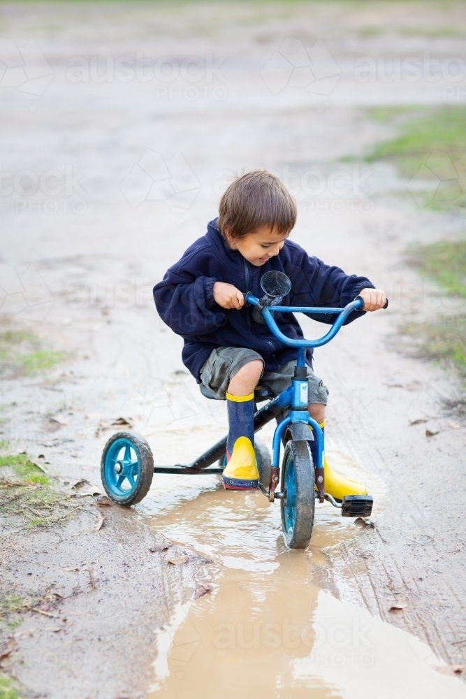 Kid riding a tricycle in puddle - Australian Stock Image