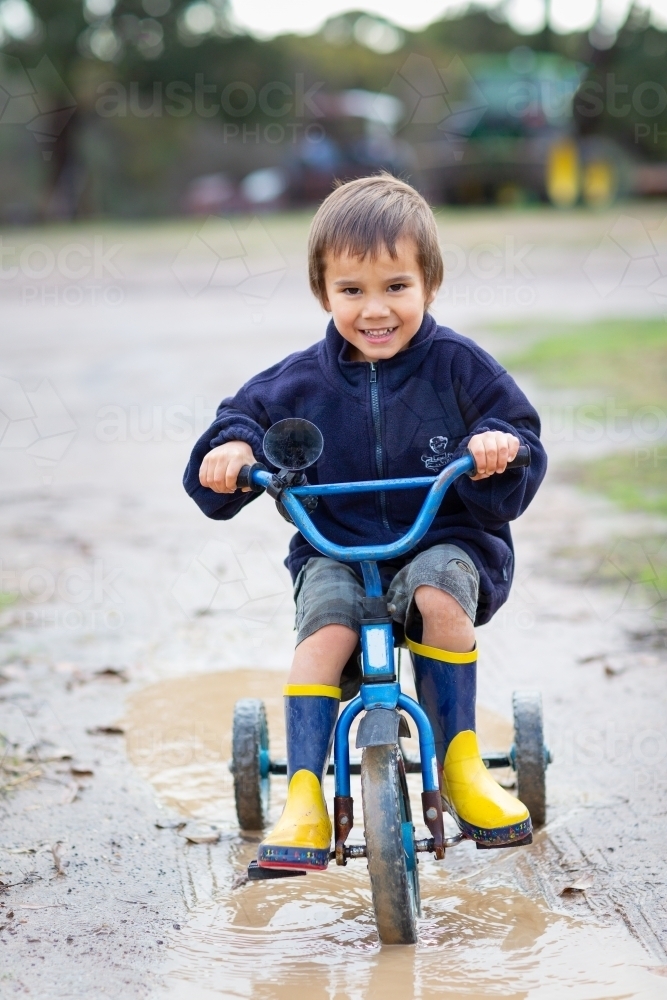 Kid riding a tricycle in puddle - Australian Stock Image