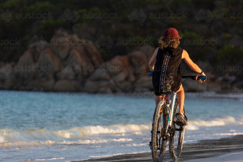 Kid riding away on a bike on the beach - Australian Stock Image