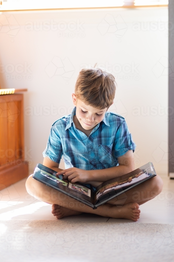 Kid sitting on the floor looking at a book - Australian Stock Image