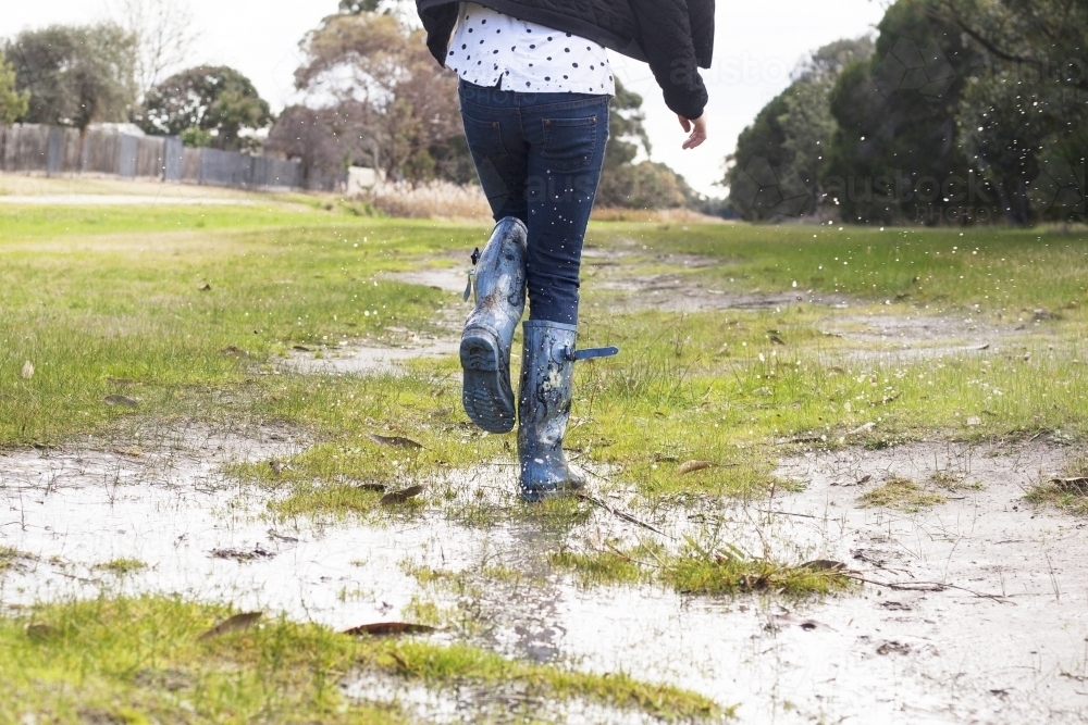 Kid splashing in puddles in gumboots on a rainy winter day. - Australian Stock Image