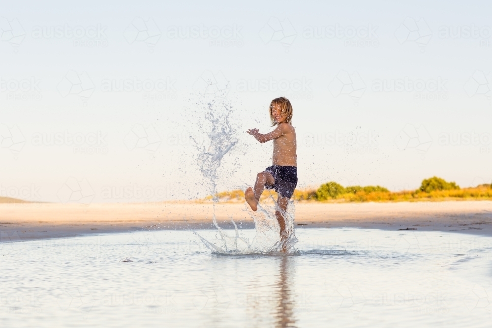 Image of Kid splashing water on the beach - Austockphoto