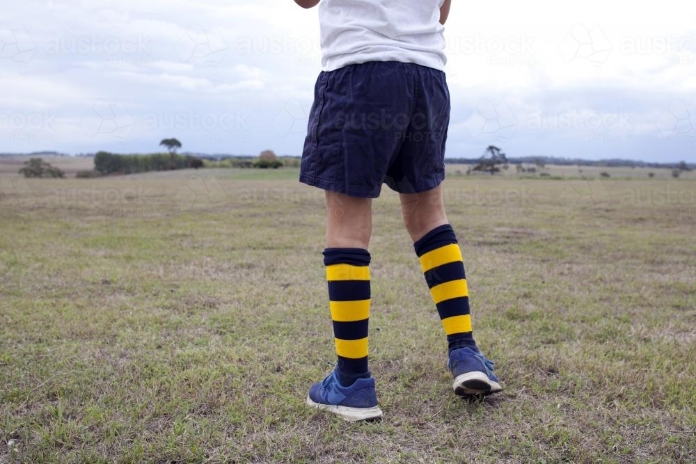 Kid standing on field wearing striped football socks - Australian Stock Image