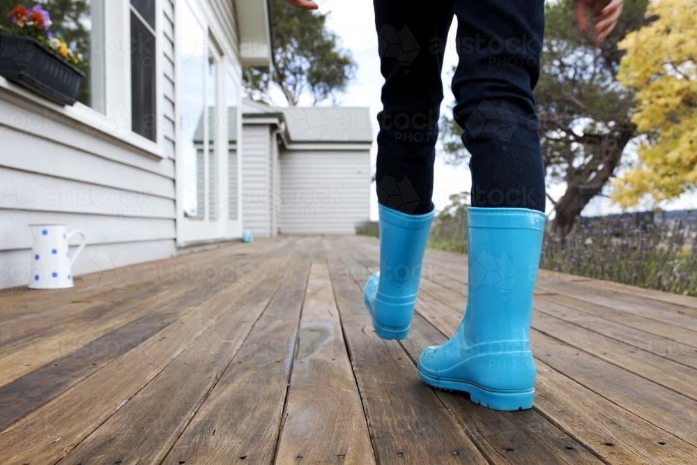Kid walking along wooden verandah in blue gumboots - Australian Stock Image