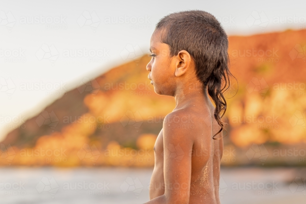 kid with rat tail haircut looking out to beach in profile against blurry landscape - Australian Stock Image
