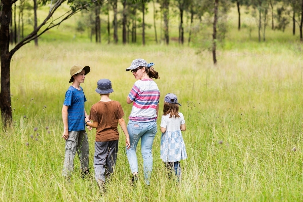 Kids and teen walking through long grass in farm paddock - Australian Stock Image