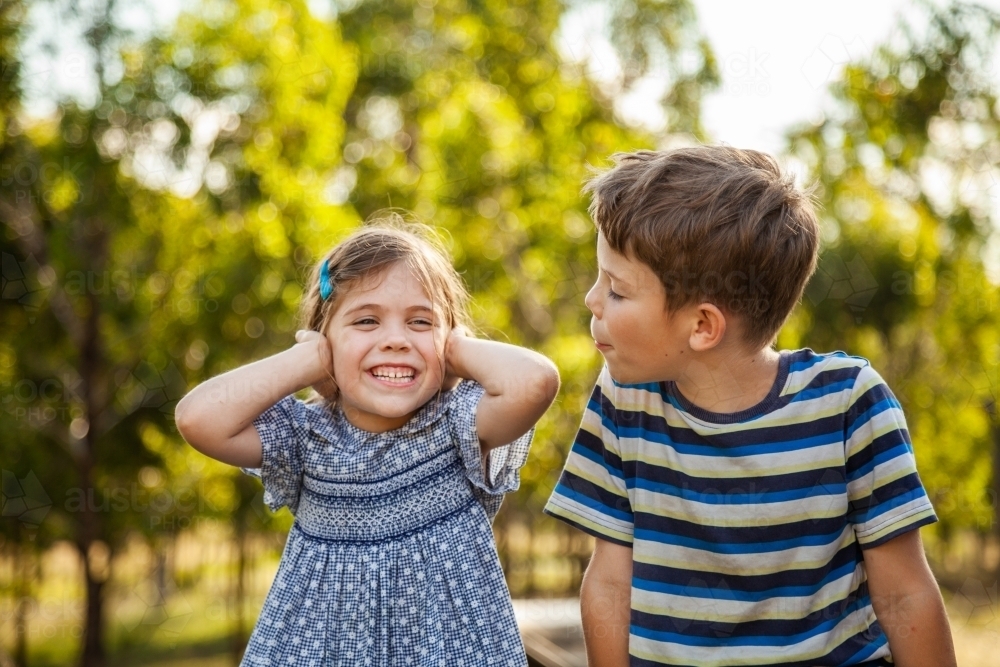 Kids being silly together - boy shouting and roaring at little girl with ears blocked not listening - Australian Stock Image