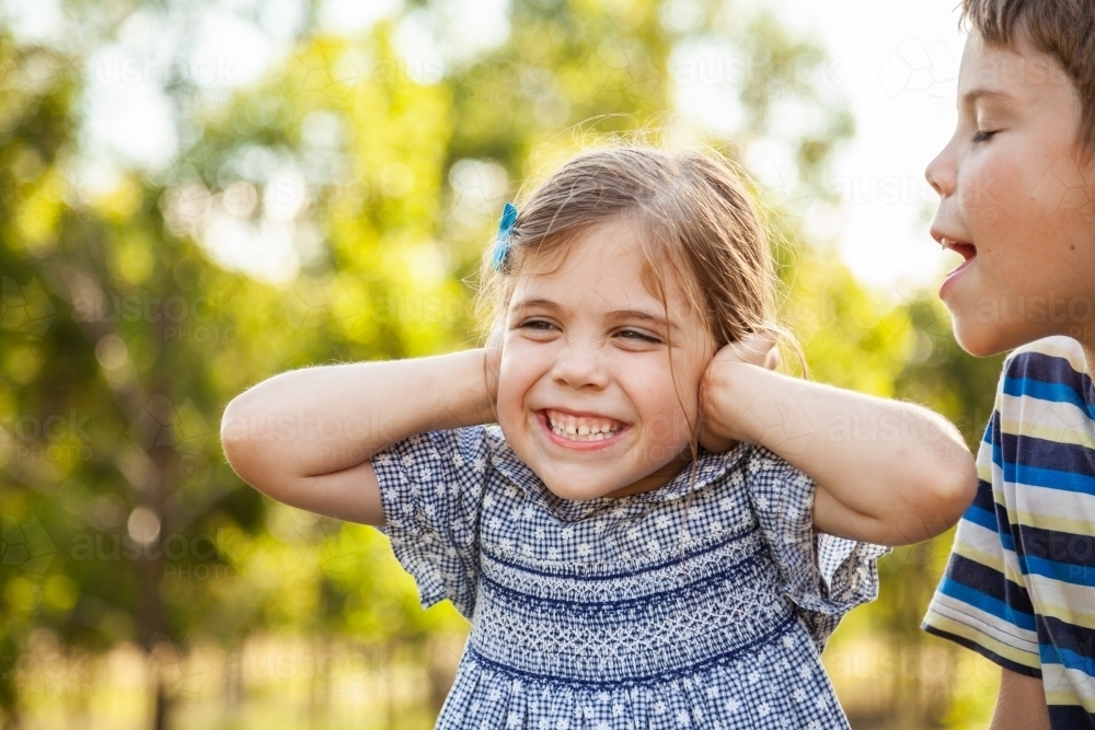 Kids being silly together - boy shouting and roaring at little girl with ears blocked not listening - Australian Stock Image
