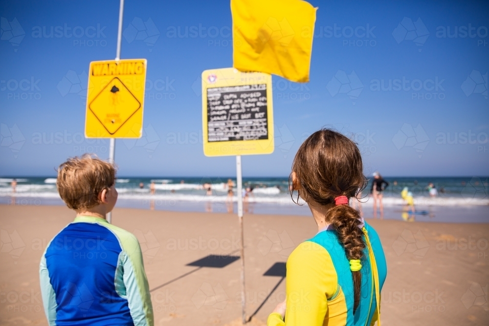 kids checking the beach report sign at the beach - Australian Stock Image