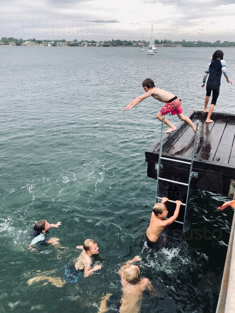 Kids climbing up ladder, out of the water, to jump off jetty - Australian Stock Image