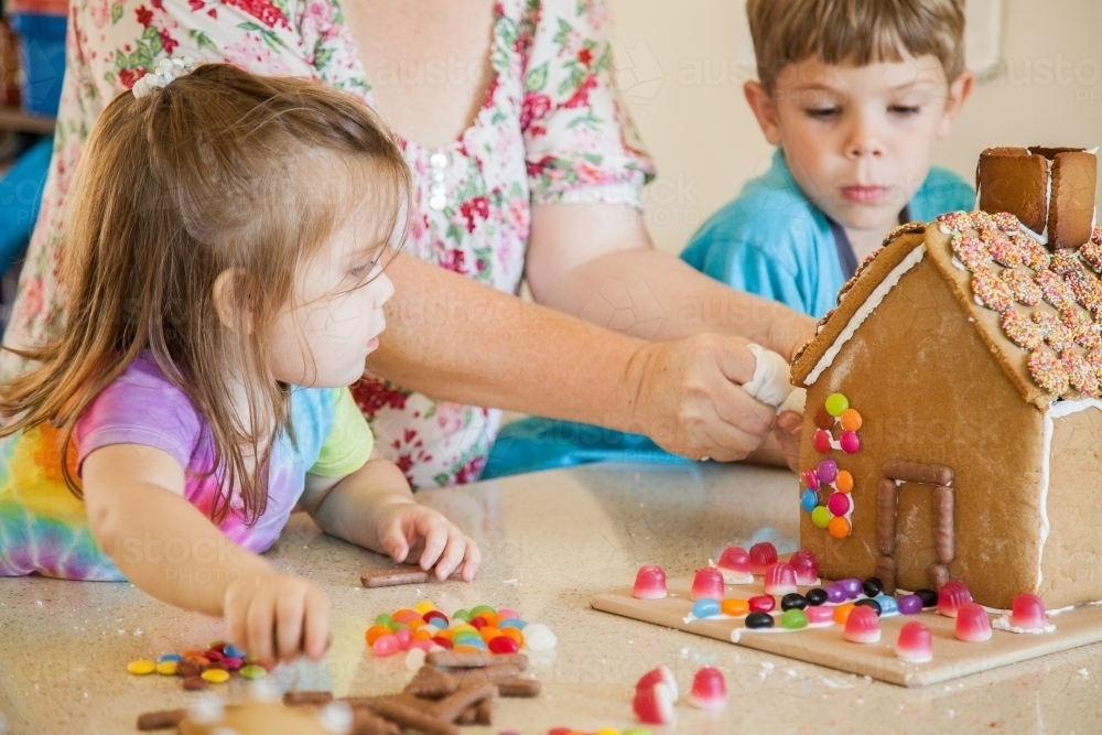 Kids decorating gingerbread house with lollies for christmas - Australian Stock Image