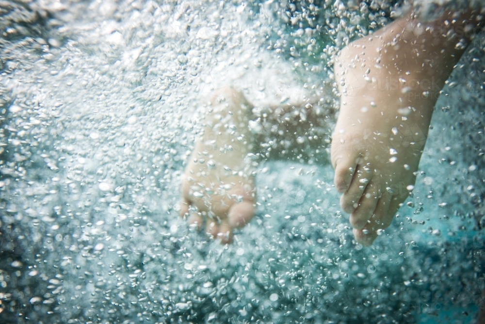Kids feet kicking while swimming in a backyard pool - Australian Stock Image