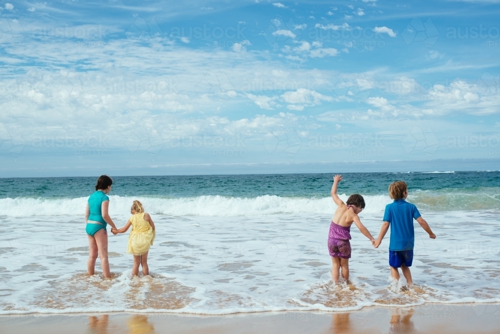 Kids holding hands in surf - Australian Stock Image